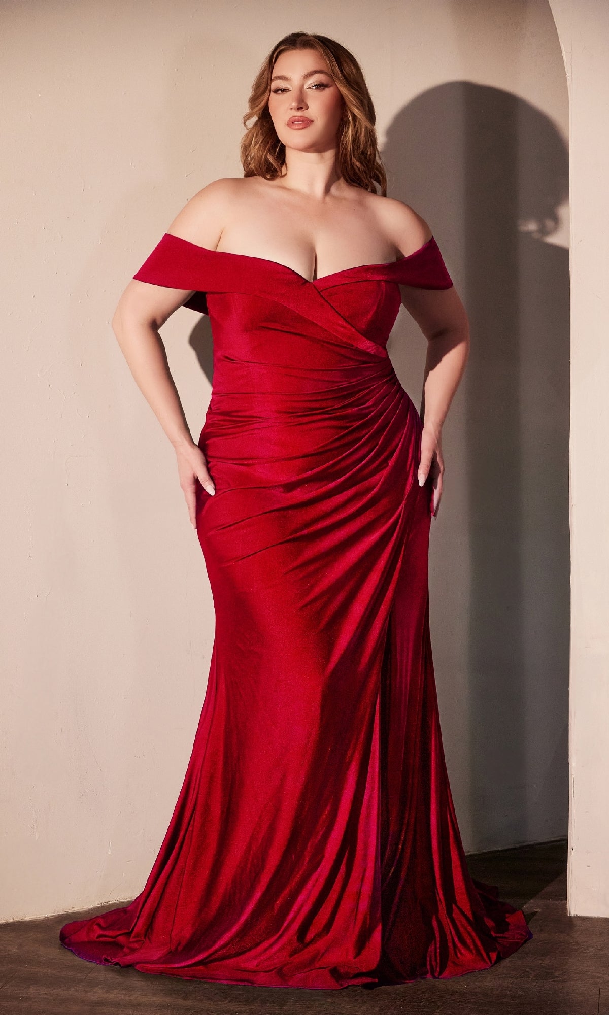 A woman poses by a light wall in the Ladivine CD790C, an off-shoulder plus-size formal prom gown—a floor-length fitted red dress ideal for evening events, all under $150.